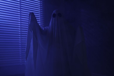 Creepy ghost. Woman covered with sheet near window in blue light