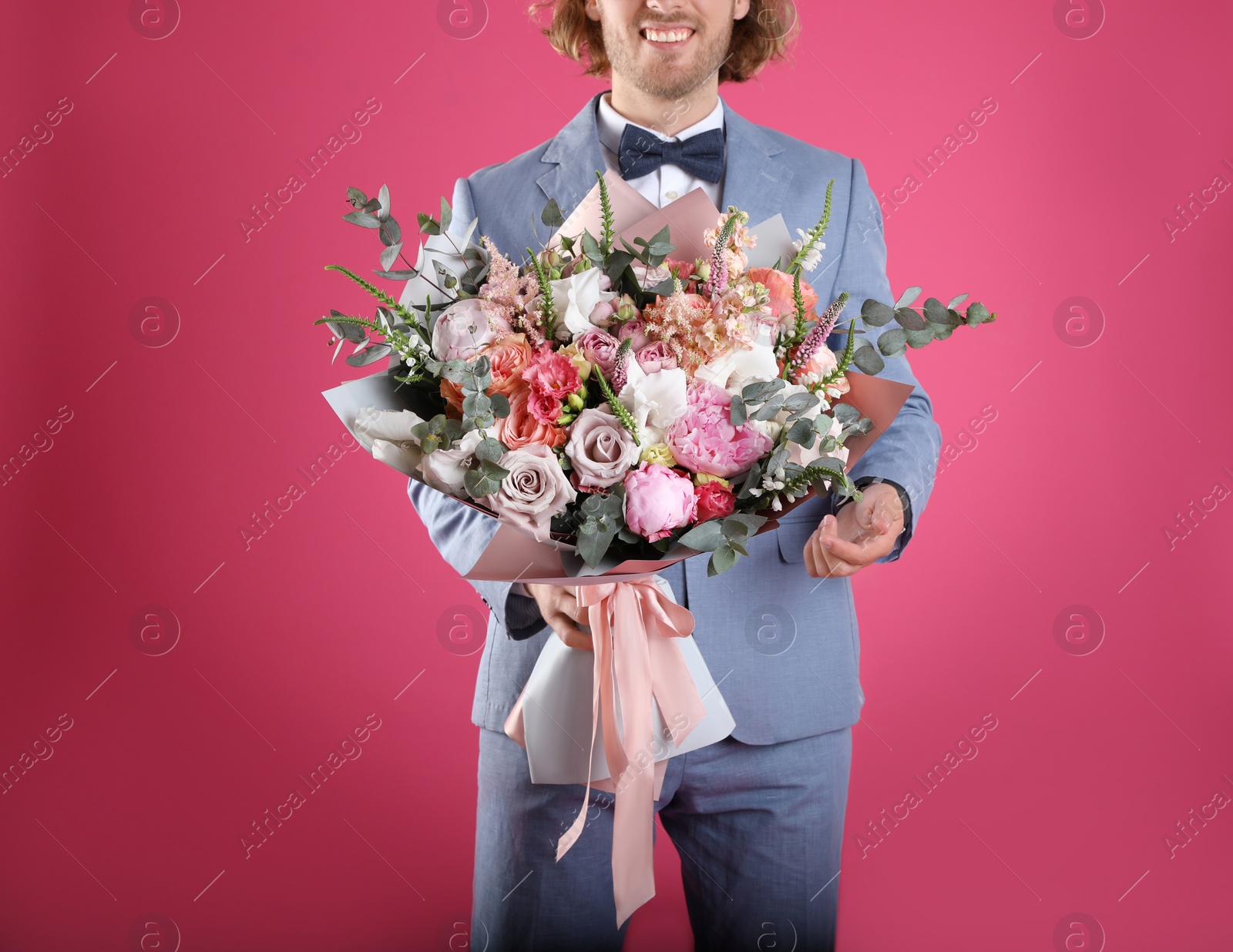 Photo of Man in stylish suit holding beautiful flower bouquet on pink background, closeup view