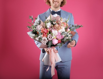 Man in stylish suit holding beautiful flower bouquet on pink background, closeup view