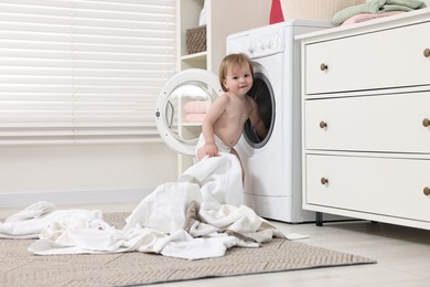 Little girl pulling baby clothes out of washing machine indoors