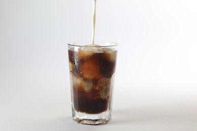 Photo of Pouring milk into glass of iced coffee on white background