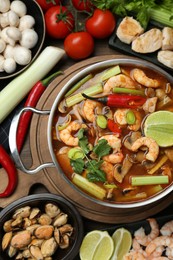 Photo of Saucepan with delicious Tom Yum soup and ingredients on wooden table, flat lay