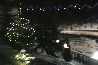 Photo of Snow globe with Christmas lights and fir trees on background outdoors