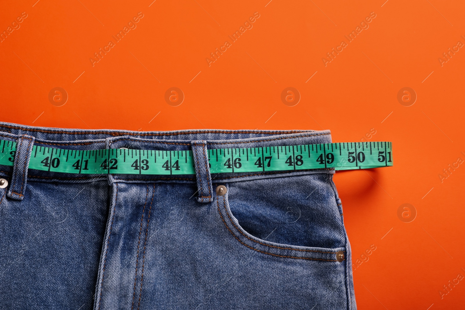 Photo of Jeans and measuring tape on orange background, top view. Weight loss concept