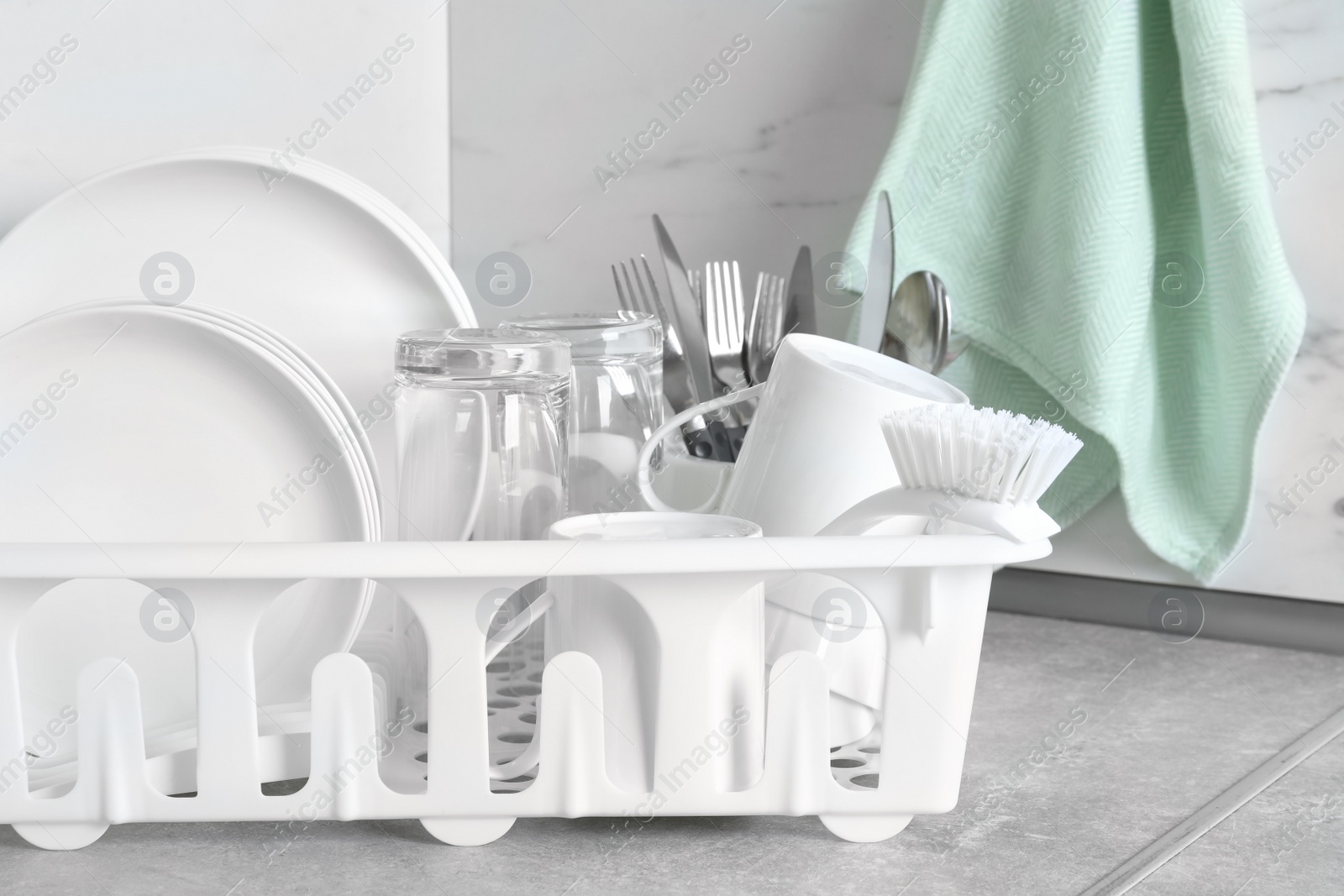 Photo of Drying rack with clean dishes and cutlery on table near light wall