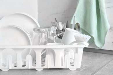 Drying rack with clean dishes and cutlery on table near light wall