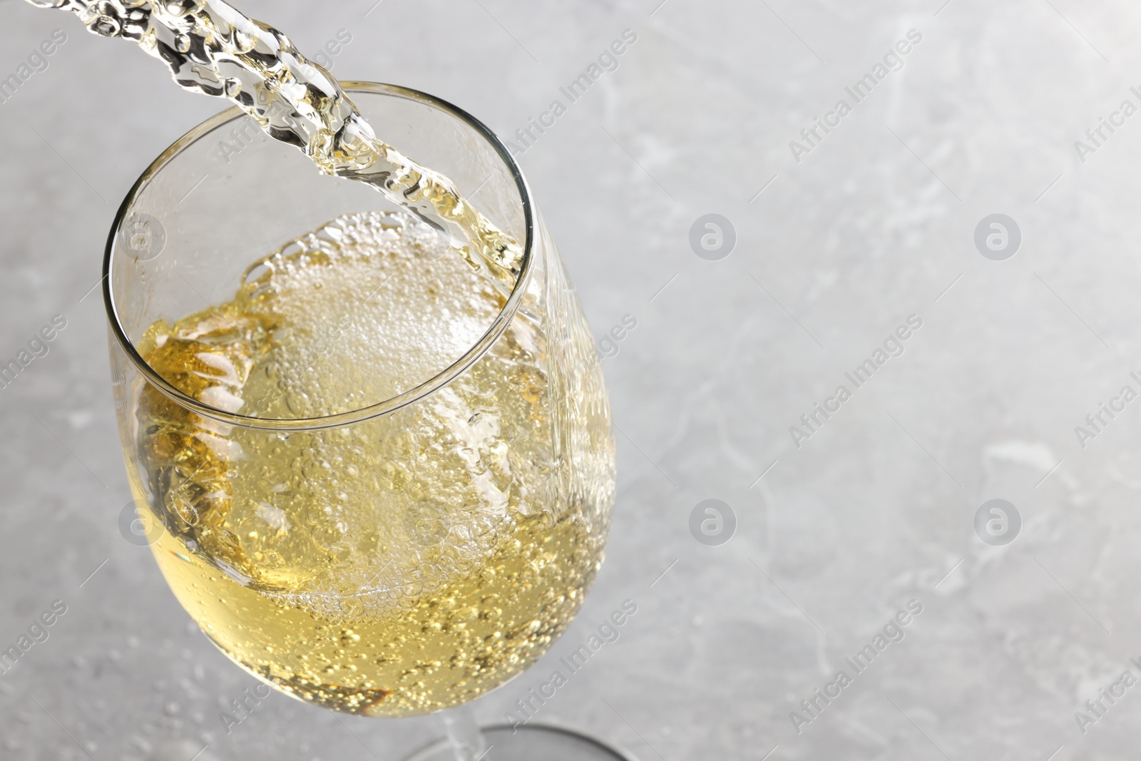 Photo of Pouring tasty aromatic wine in glass at gray marble table, closeup. Space for text