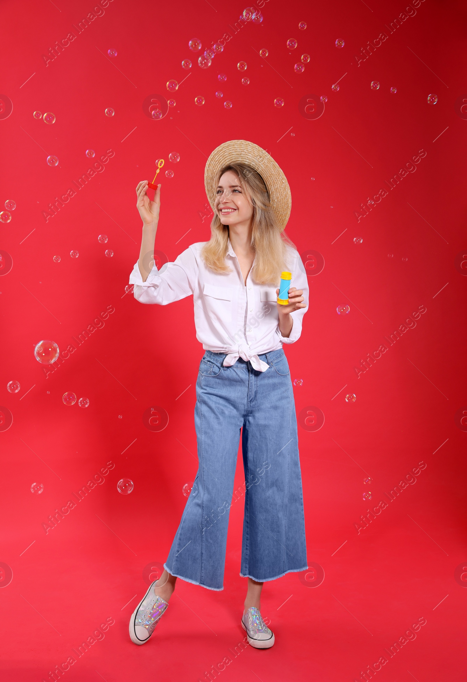 Photo of Young woman blowing soap bubbles on red background