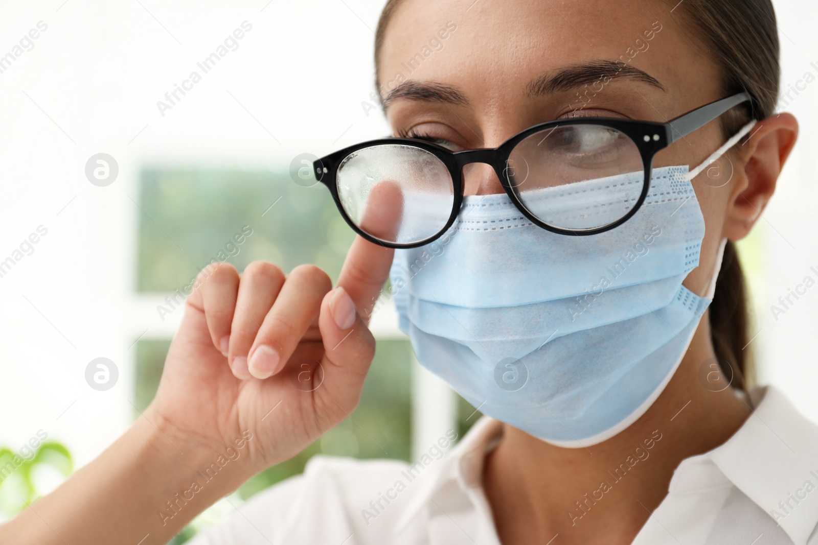 Photo of Woman wiping foggy glasses caused by wearing medical mask indoors, closeup