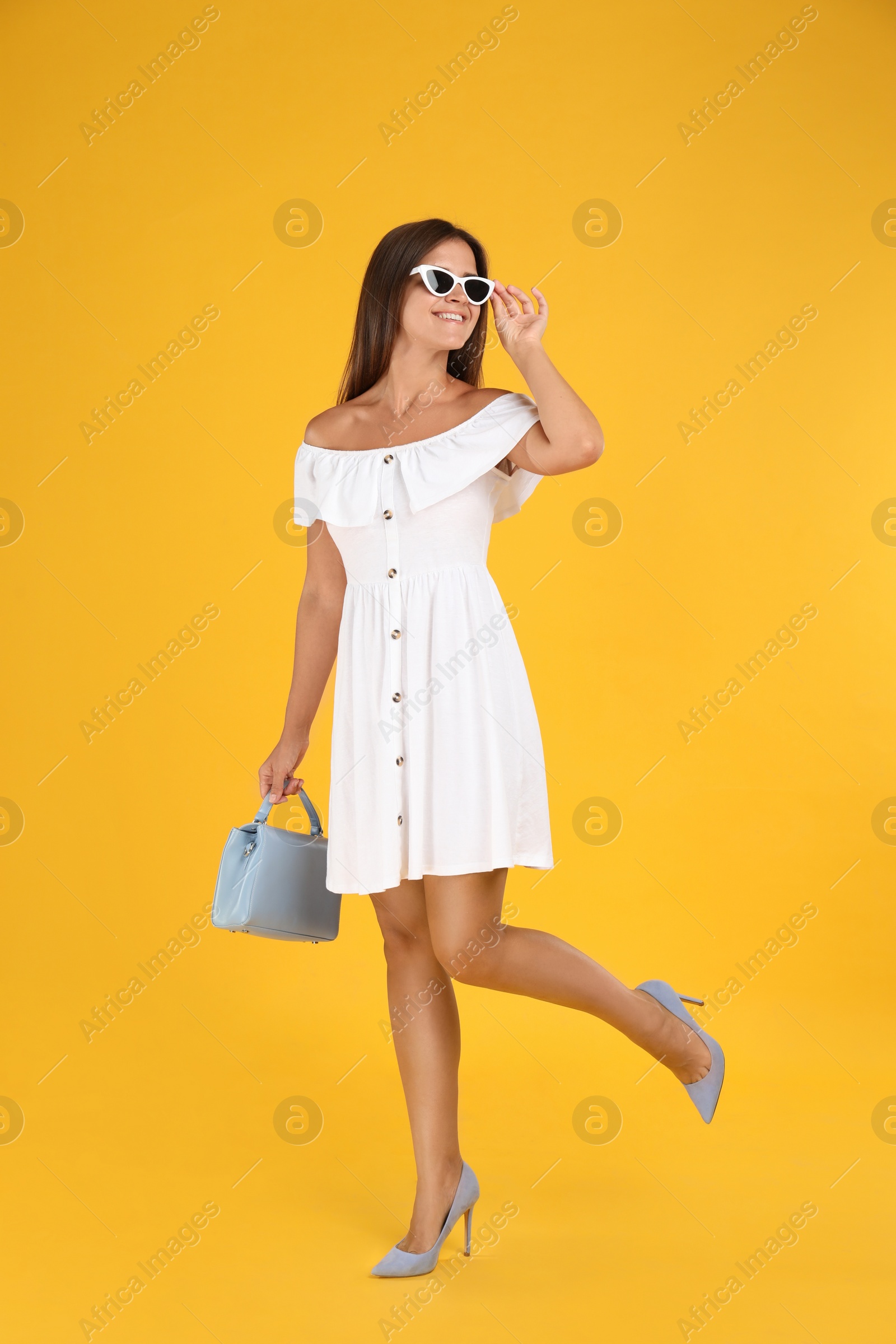 Photo of Young woman wearing stylish white dress with elegant bag on yellow background