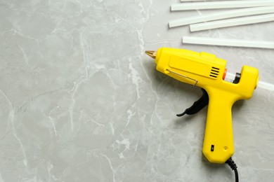 Yellow glue gun and sticks on light grey marble table, flat lay. Space for text