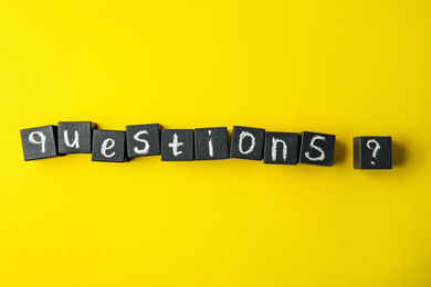 Photo of Word QUESTIONS and query mark with black cubes on yellow background, flat lay