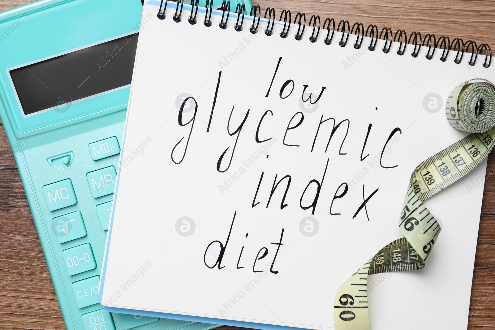 Photo of Notebook with words Low Glycemic Index Diet, measuring tape and calculator on wooden table, flat lay