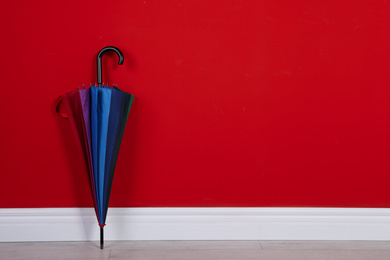 Photo of Beautiful colorful umbrella near red wall. Space for text