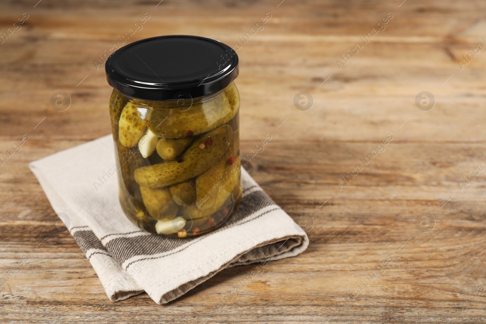 Photo of Tasty pickled cucumbers in glass jar on wooden table, space for text