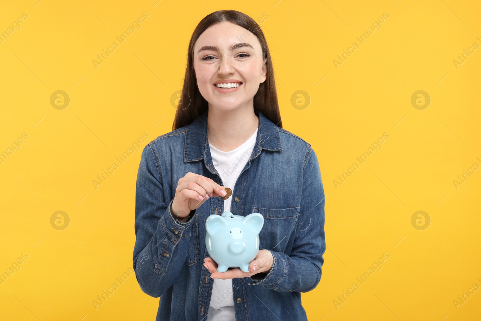 Photo of Happy woman putting coin into piggy bank on orange background