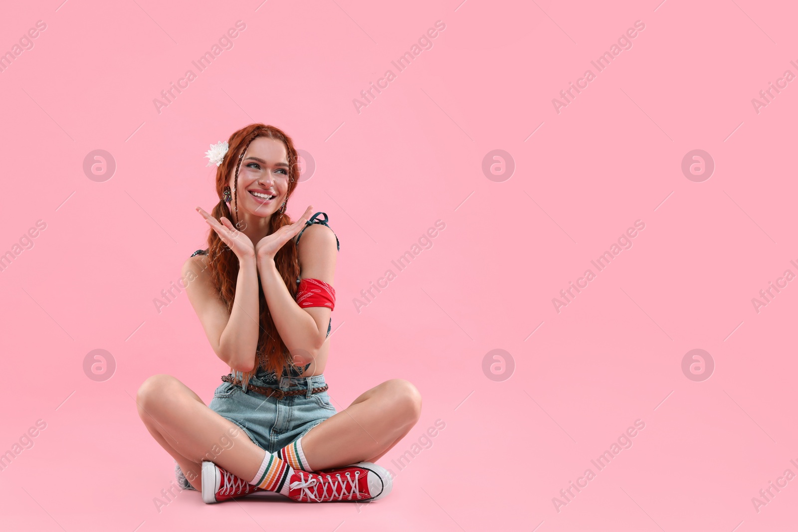 Photo of Beautiful young hippie woman sitting on pink background, space for text