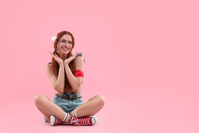 Beautiful young hippie woman sitting on pink background, space for text