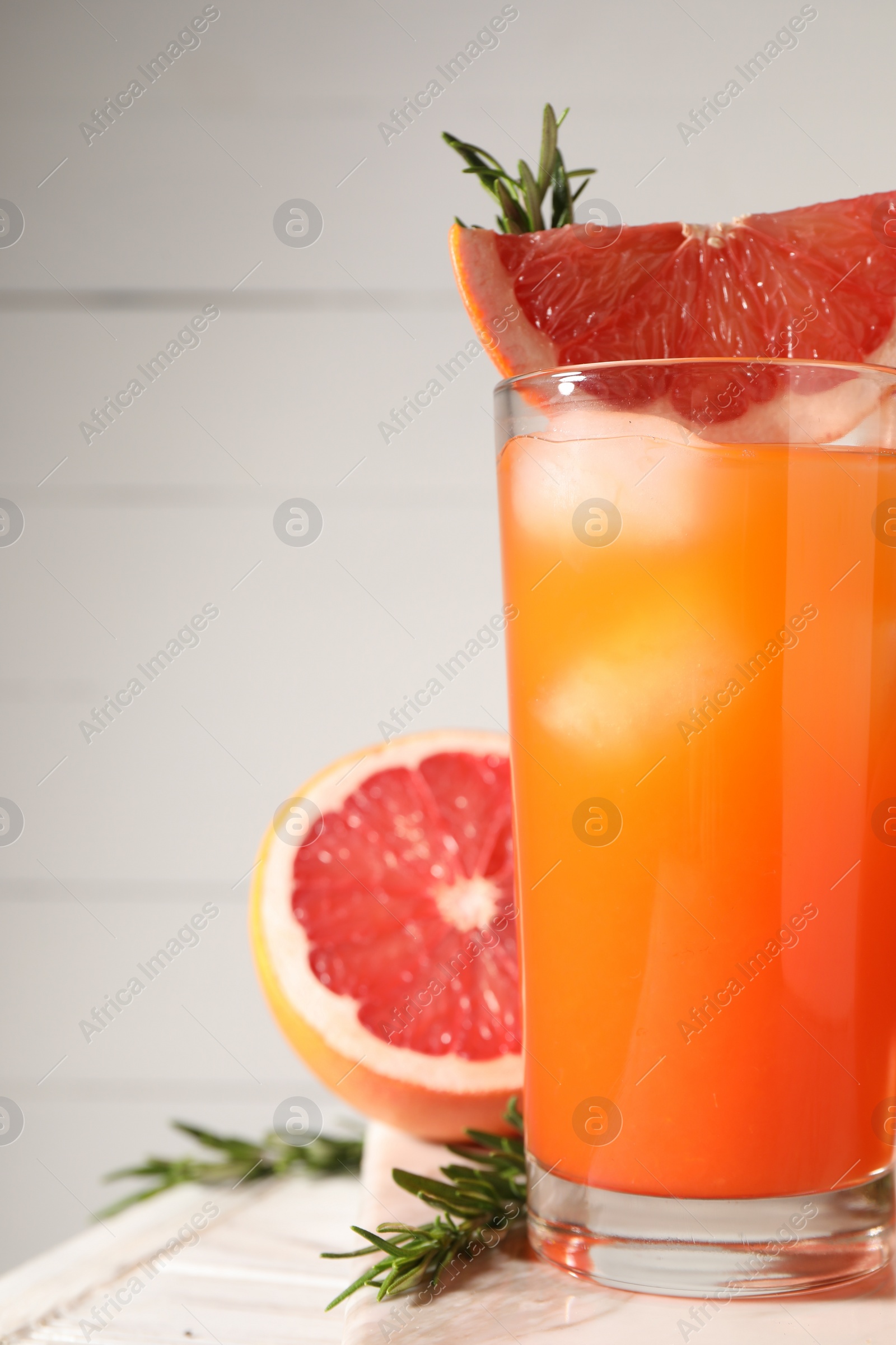 Photo of Tasty grapefruit drink with ice in glass, rosemary and fresh fruit on light table, closeup. Space for text