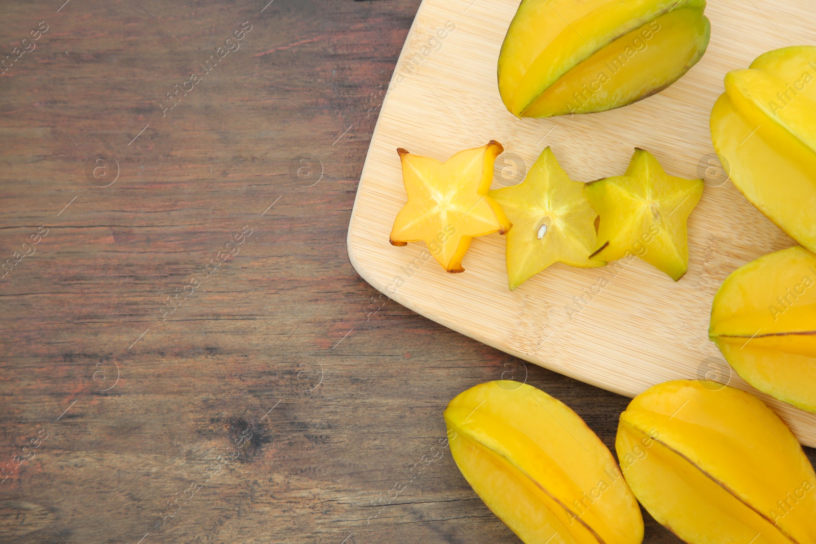 Photo of Cut and whole delicious ripe carambolas on wooden table, flat lay. Space for text