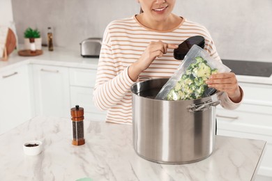 Photo of Woman putting vacuum packed broccoli into pot and using thermal immersion circulator, closeup. Sous vide cooking