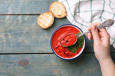 Photo of Woman eating delicious tomato cream soup at light blue wooden table, top view. Space for text