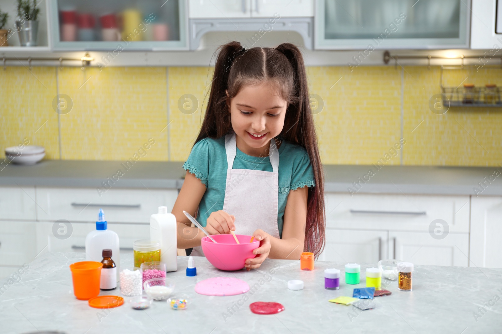 Photo of Cute little girl making homemade slime toy at table in kitchen