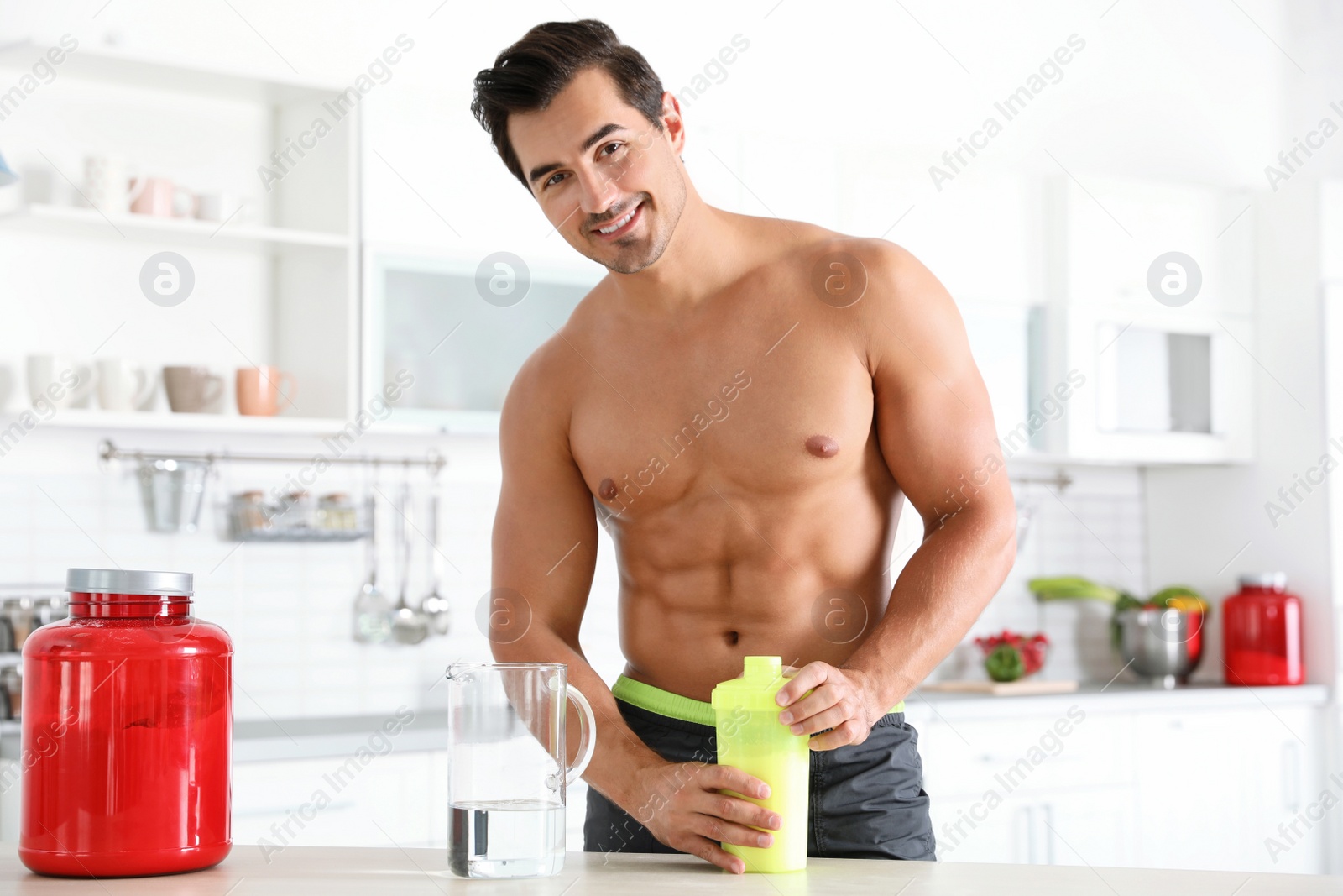 Photo of Young shirtless athletic man with protein shake powder in kitchen