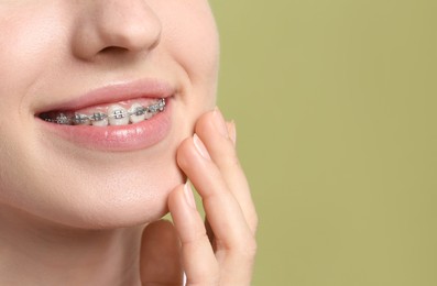 Photo of Smiling woman with dental braces on light green background, closeup. Space for text