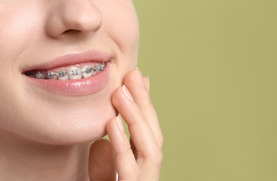 Smiling woman with dental braces on light green background, closeup. Space for text