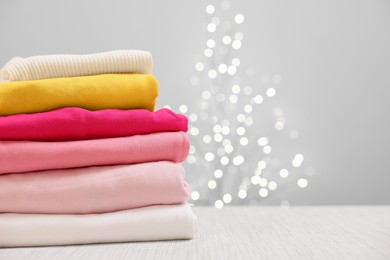 Photo of Stack of folded clothes on wooden table against beige background with blurred lights, space for text