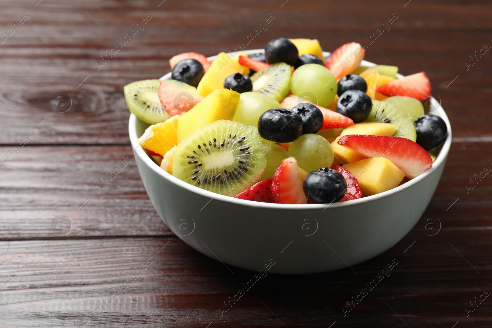 Photo of Tasty fruit salad in bowl on wooden table, closeup