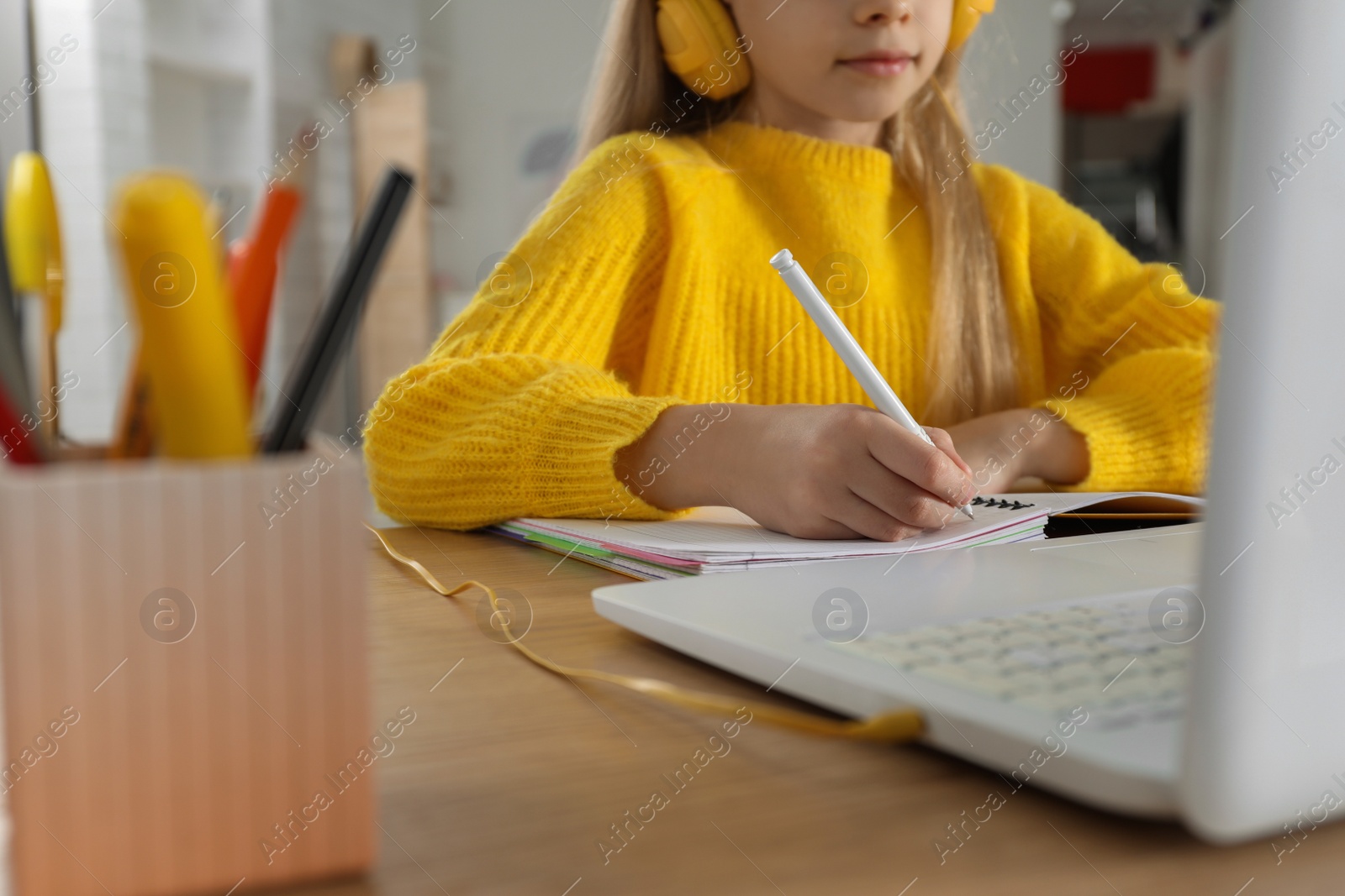 Photo of Cute little girl with modern laptop studying online at home, closeup. E-learning