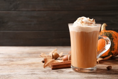 Glass cup with tasty pumpkin spice latte on wooden table. Space for text