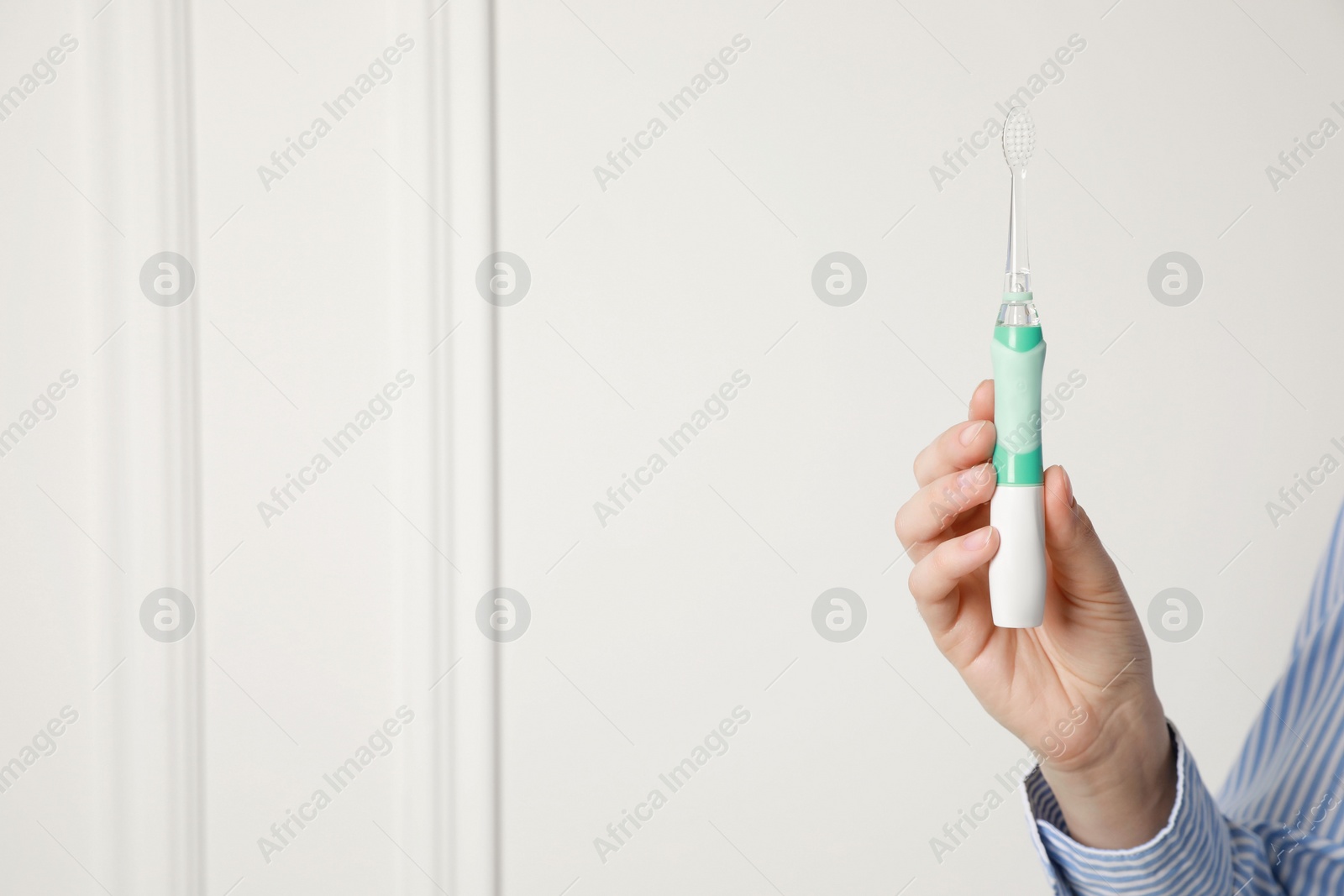 Photo of Woman holding electric toothbrush near white wall, closeup. Space for text