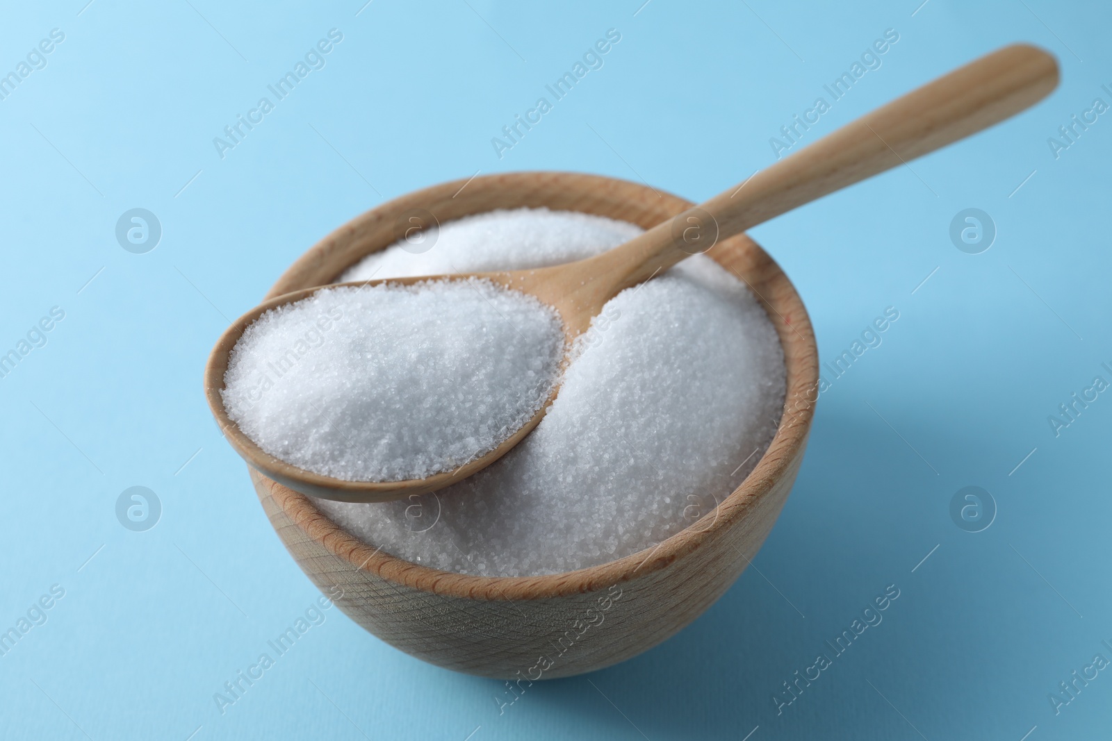 Photo of Organic white salt in bowl and spoon on light blue background, closeup