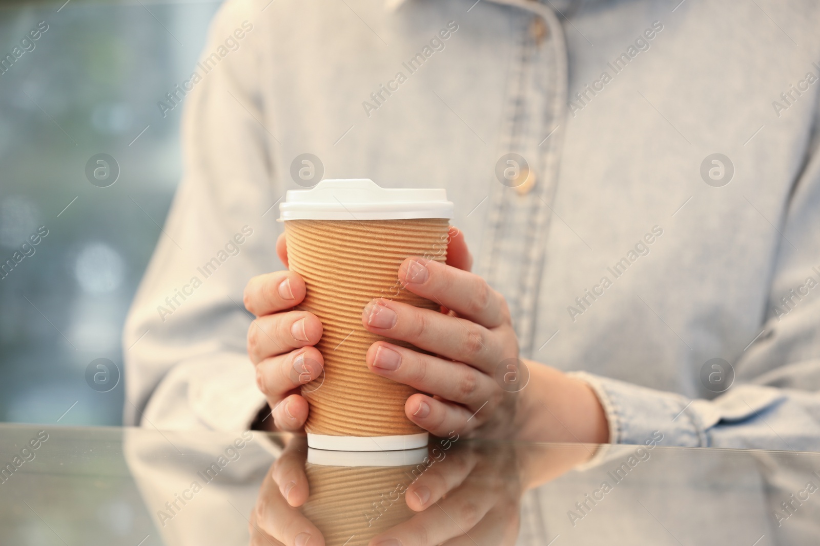 Photo of Woman holding takeaway paper cup at table, closeup. Coffee to go