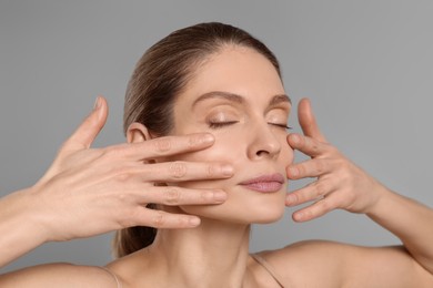 Photo of Woman massaging her face on grey background