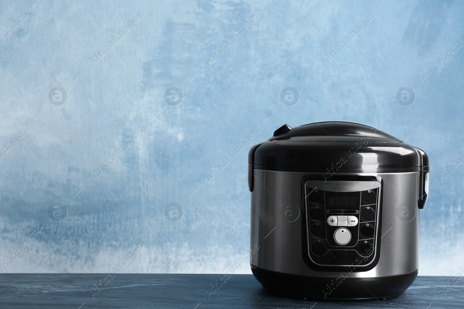 Photo of Modern powerful multi cooker on table against color background. Space for text