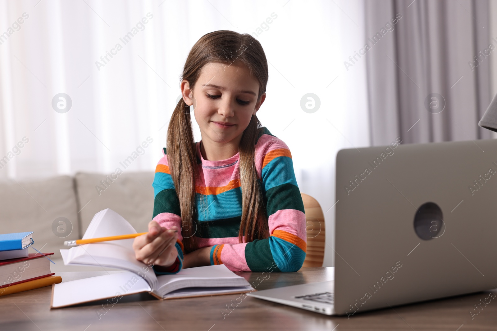 Photo of E-learning. Cute girl taking notes during online lesson at table indoors