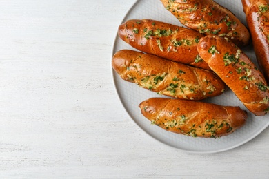 Photo of Plate of bread loaves with garlic and herbs on white wooden table, top view. Space for text