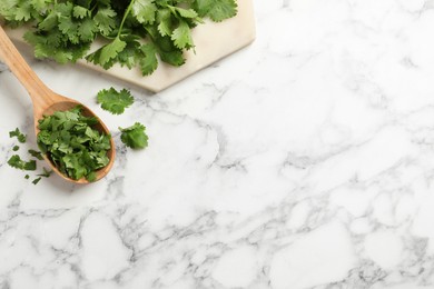 Photo of Fresh green cilantro and wooden spoon on white marble table, flat lay. Space for text