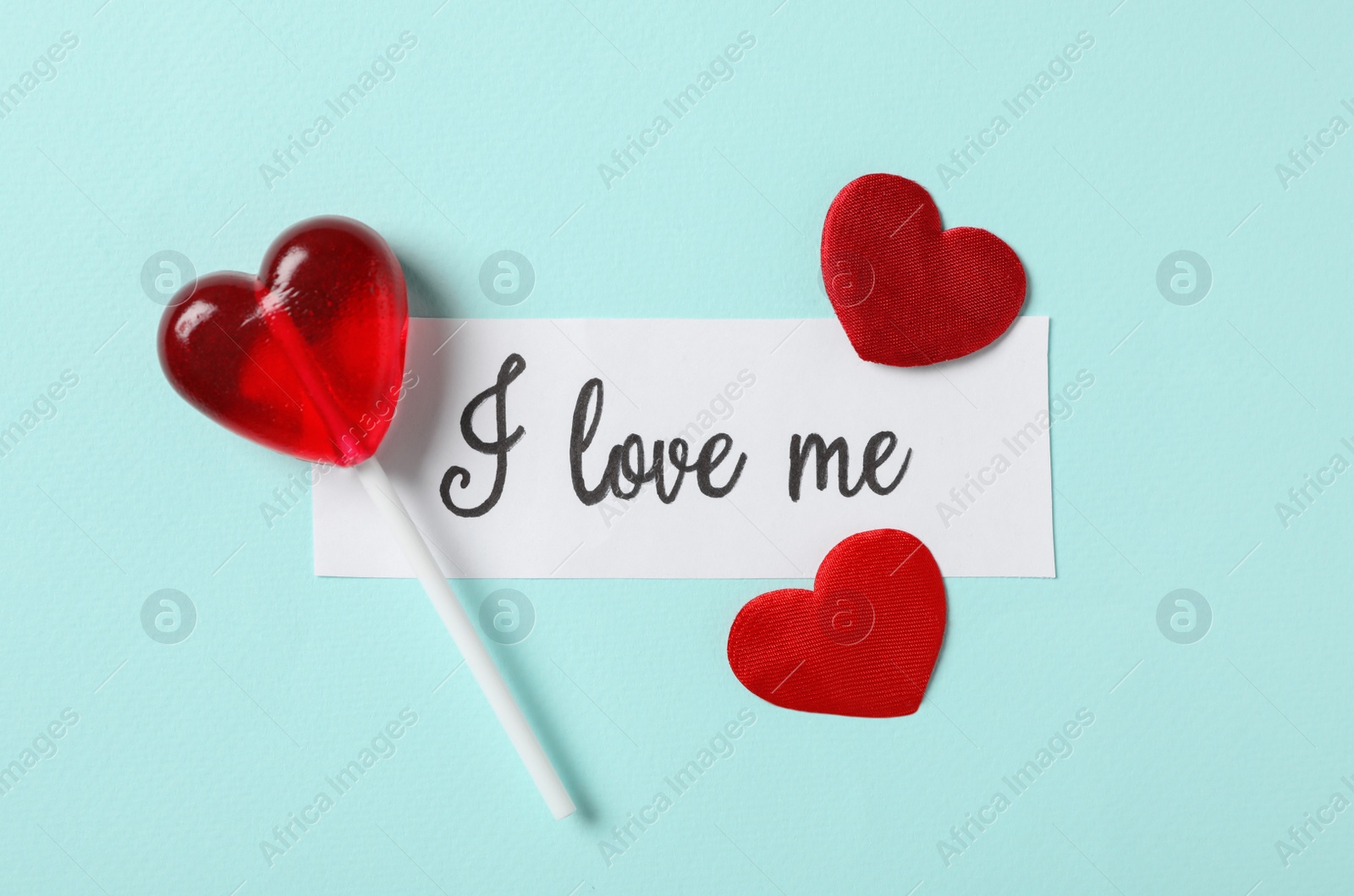 Photo of Piece of paper with handwritten phrase I Love Me, lollipop and hearts on turquoise background, flat lay