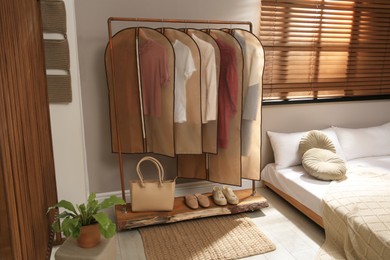 Photo of Garment bags with clothes hanging on rack in bedroom