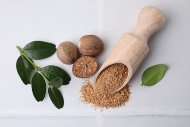 Scoop with grated nutmeg, seeds and green leaves on white table, flat lay