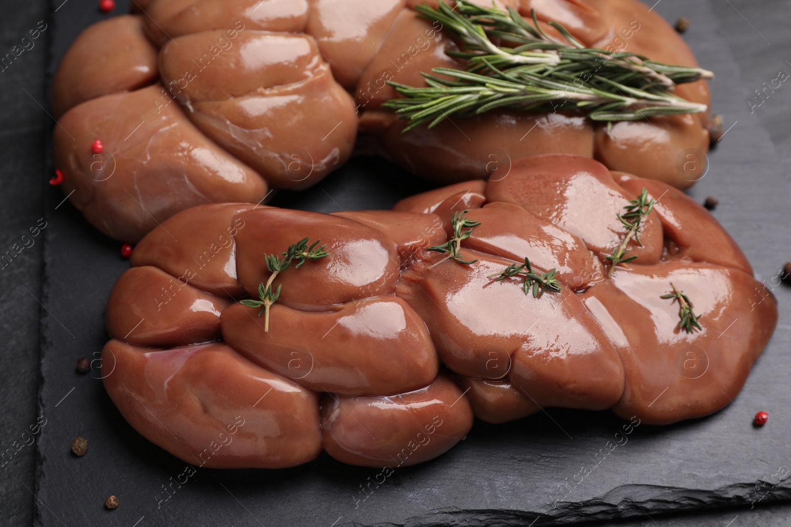 Photo of Fresh raw kidneys with rosemary and thyme on black table, closeup