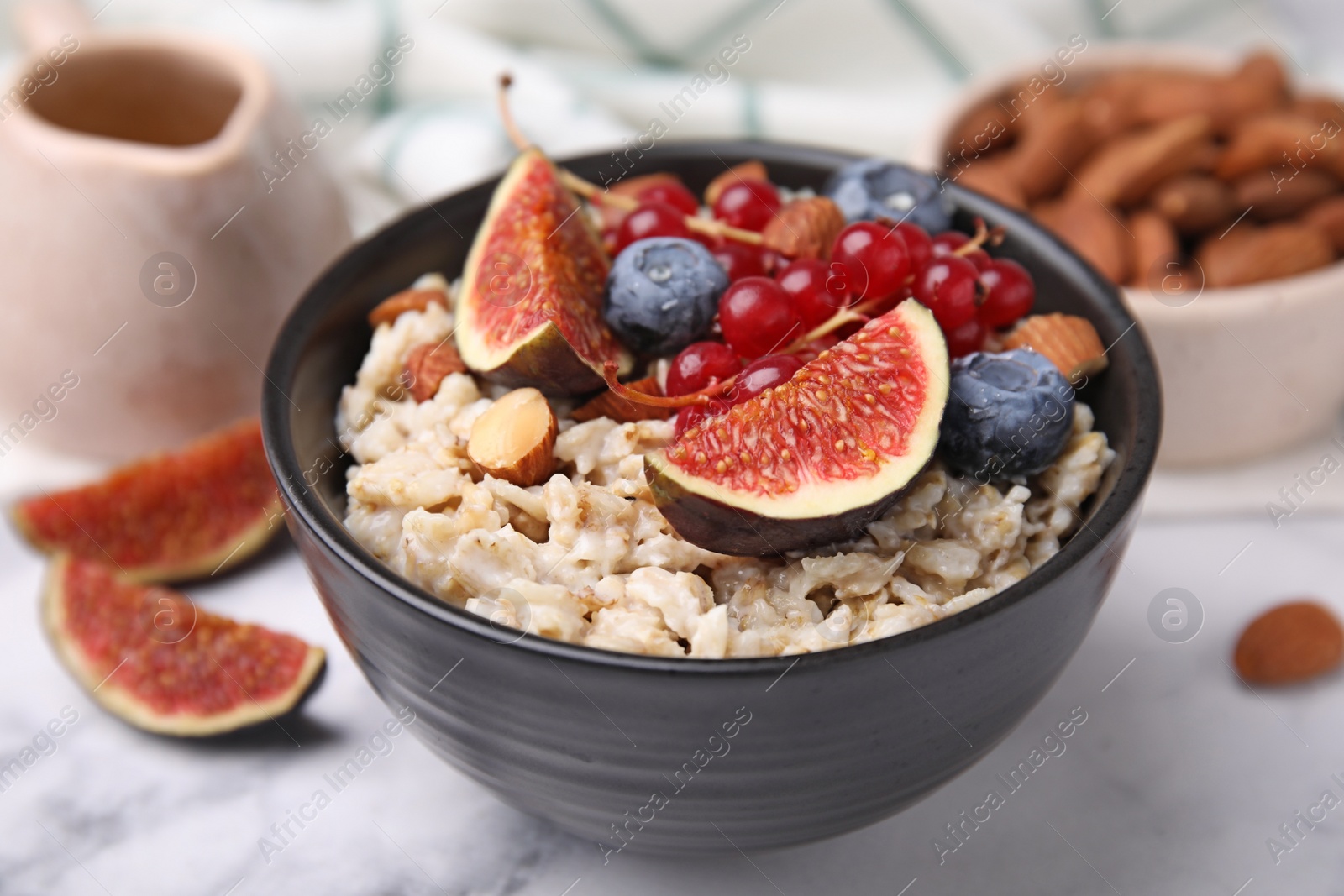Photo of Bowl of oatmeal with berries, almonds and fig pieces on white marble table, closeup