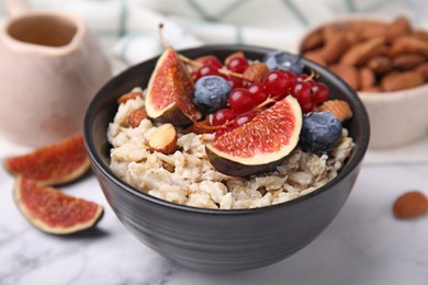 Bowl of oatmeal with berries, almonds and fig pieces on white marble table, closeup