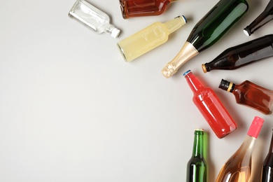 Bottles with different alcoholic drinks on light background, top view. Space for text