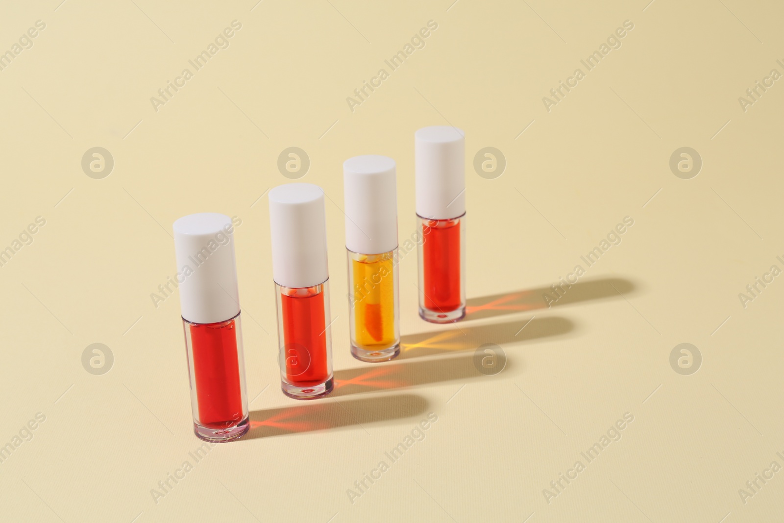 Photo of Bright lip glosses on beige background, space for text